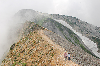 鑓ヶ岳を背に杓子岳の山頂直下を歩いている写真